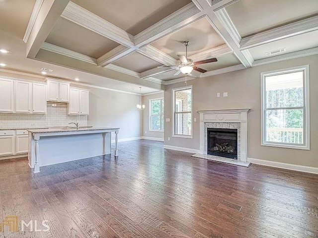 unfurnished living room with coffered ceiling, a fireplace, plenty of natural light, and dark wood finished floors