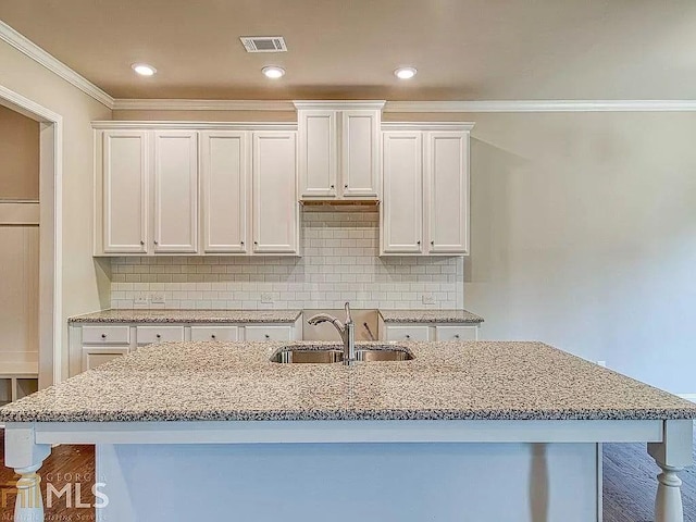 kitchen featuring a sink, visible vents, white cabinets, backsplash, and an island with sink