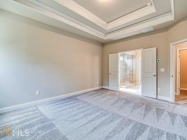 empty room with carpet floors, a tray ceiling, crown molding, and baseboards