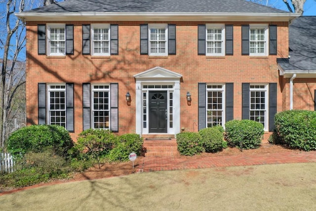 colonial home featuring brick siding and roof with shingles