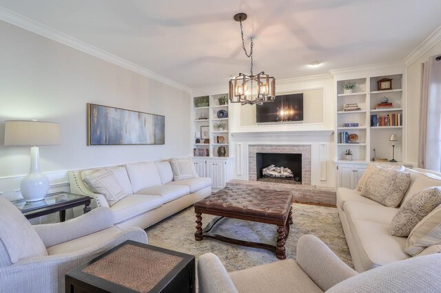 living area with built in features, a brick fireplace, a chandelier, and ornamental molding