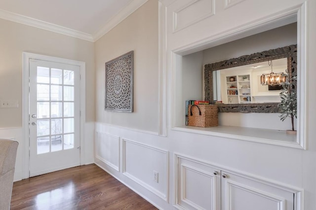 doorway featuring dark wood-type flooring, ornamental molding, built in features, an inviting chandelier, and wainscoting