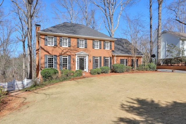 colonial house featuring brick siding, a chimney, and fence