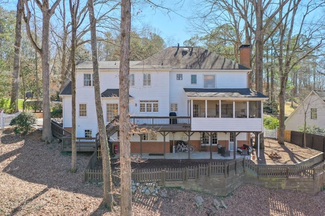 back of property featuring a fenced backyard, a sunroom, a chimney, a deck, and a patio area