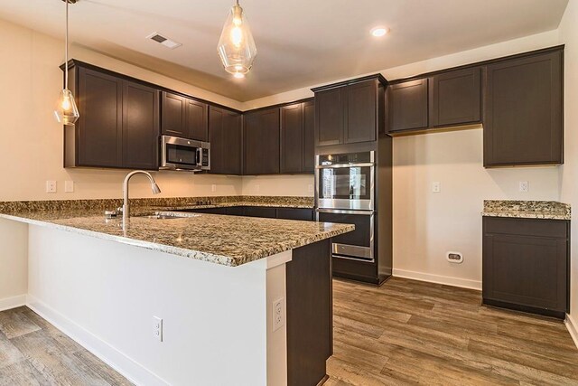 kitchen featuring a peninsula, stainless steel appliances, dark brown cabinets, stone counters, and a sink