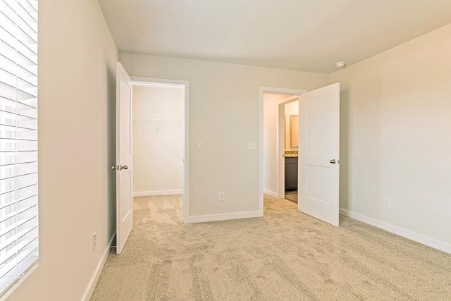 unfurnished bedroom with a walk in closet, a closet, light colored carpet, and baseboards