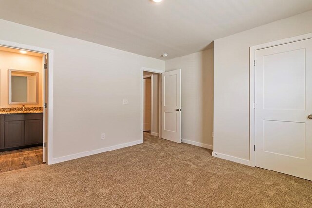 unfurnished bedroom with light carpet, baseboards, a sink, and ensuite bathroom