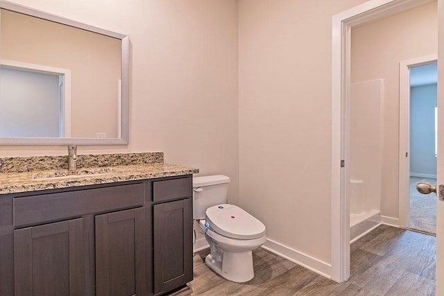 bathroom featuring a shower, toilet, vanity, wood finished floors, and baseboards