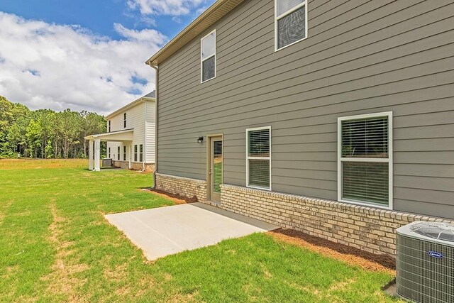 rear view of property with cooling unit, brick siding, a lawn, and a patio