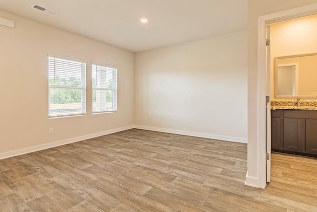 unfurnished room featuring light wood-style floors, baseboards, visible vents, and a sink