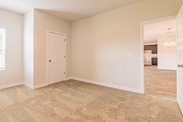 empty room featuring light carpet, baseboards, and an inviting chandelier