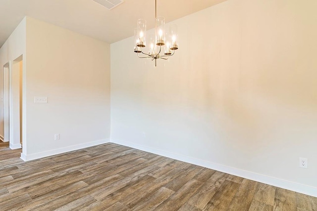 unfurnished room featuring visible vents, a notable chandelier, baseboards, and wood finished floors