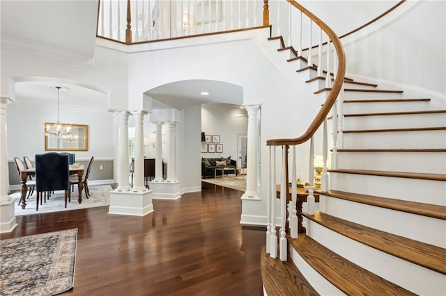 stairway with decorative columns, ornamental molding, a chandelier, hardwood / wood-style flooring, and a high ceiling