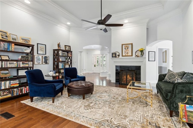 living room featuring hardwood / wood-style flooring, a tile fireplace, ceiling fan, ornamental molding, and a towering ceiling