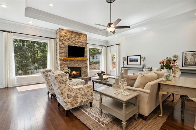 living room featuring dark hardwood / wood-style flooring, a fireplace, a tray ceiling, crown molding, and ceiling fan