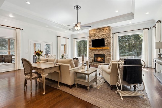 living room featuring crown molding, ceiling fan, a stone fireplace, dark hardwood / wood-style floors, and a raised ceiling