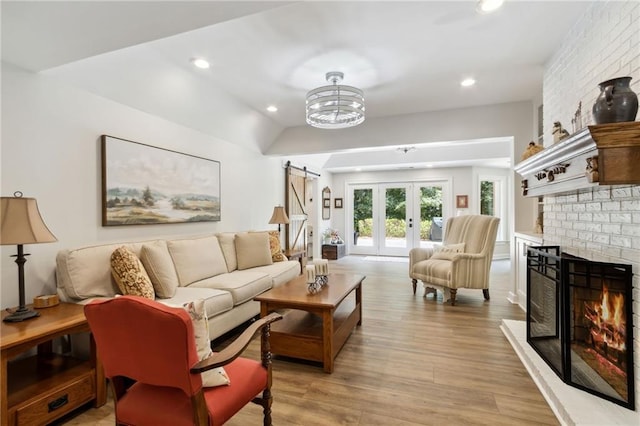 living room featuring a fireplace, light wood-type flooring, an inviting chandelier, french doors, and a barn door