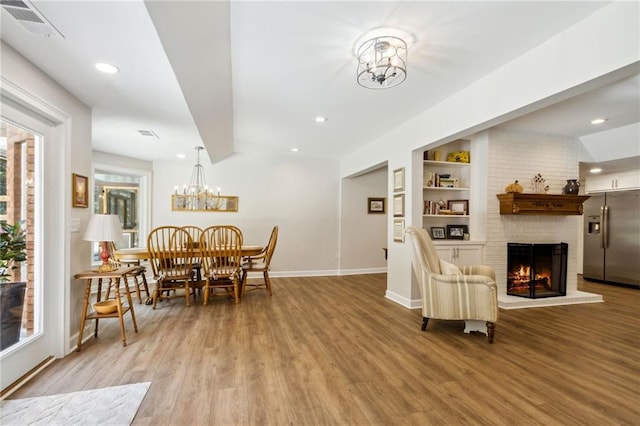 dining room with built in features, an inviting chandelier, a brick fireplace, and hardwood / wood-style flooring