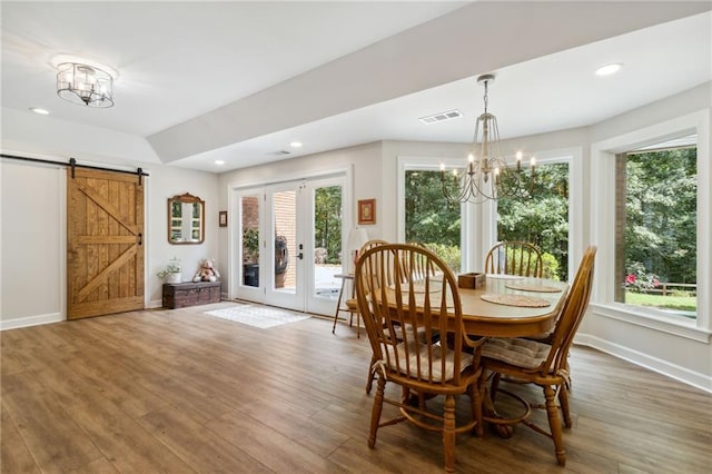 dining area with a barn door, hardwood / wood-style floors, plenty of natural light, and an inviting chandelier