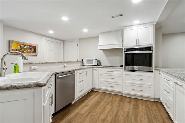 kitchen with light wood-type flooring, white cabinetry, sink, appliances with stainless steel finishes, and custom range hood