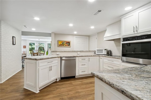 kitchen with wood-type flooring, kitchen peninsula, light stone countertops, appliances with stainless steel finishes, and white cabinets