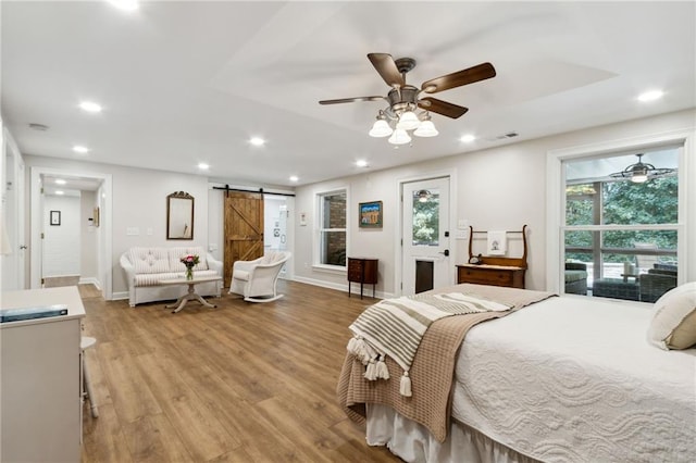 bedroom featuring a barn door, ceiling fan, and light hardwood / wood-style flooring