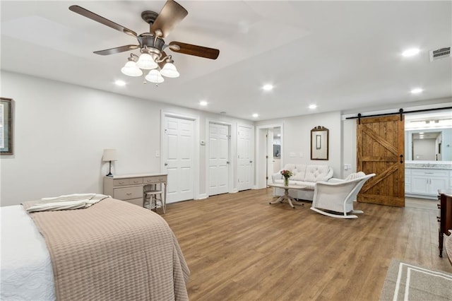 bedroom with light hardwood / wood-style flooring, ensuite bath, ceiling fan, two closets, and a barn door