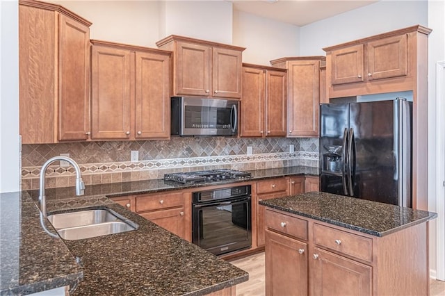 kitchen with light wood-type flooring, tasteful backsplash, dark stone counters, sink, and black appliances