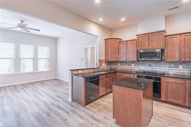 kitchen with sink, kitchen peninsula, dark stone counters, black appliances, and light wood-type flooring