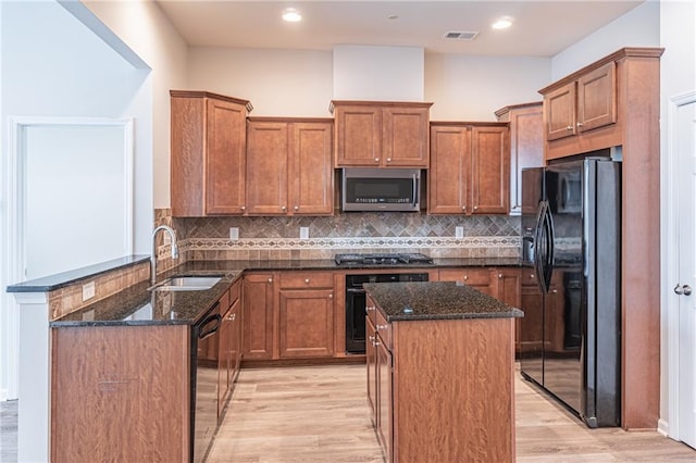 kitchen featuring dark stone countertops, black appliances, and light wood-type flooring