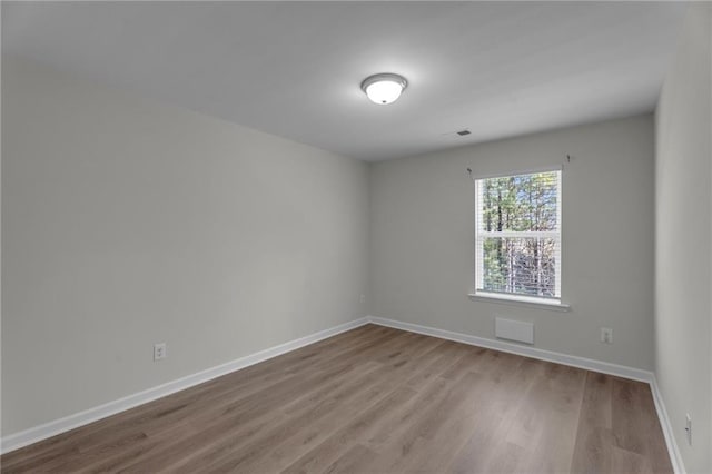 spare room with wood finished floors, visible vents, and baseboards