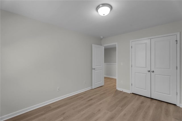 unfurnished bedroom featuring light wood-type flooring, baseboards, and a closet