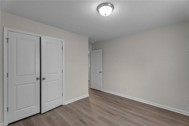 unfurnished bedroom with a closet, wood finished floors, and baseboards