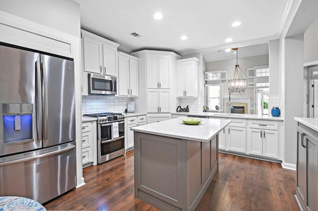 kitchen with dark hardwood / wood-style flooring, a notable chandelier, backsplash, appliances with stainless steel finishes, and white cabinets