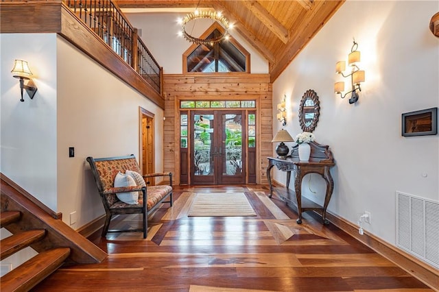 foyer entrance with visible vents, wood walls, hardwood / wood-style flooring, beamed ceiling, and stairs
