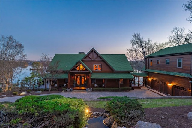 back of property at dusk featuring a garage, a porch, driveway, and metal roof