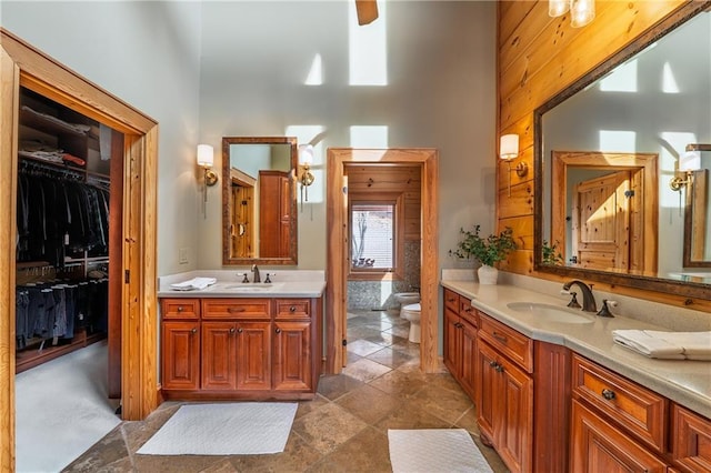 bathroom with two vanities, toilet, a high ceiling, and a sink