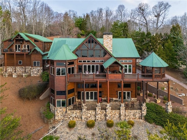 back of house featuring metal roof, french doors, stone siding, and a chimney