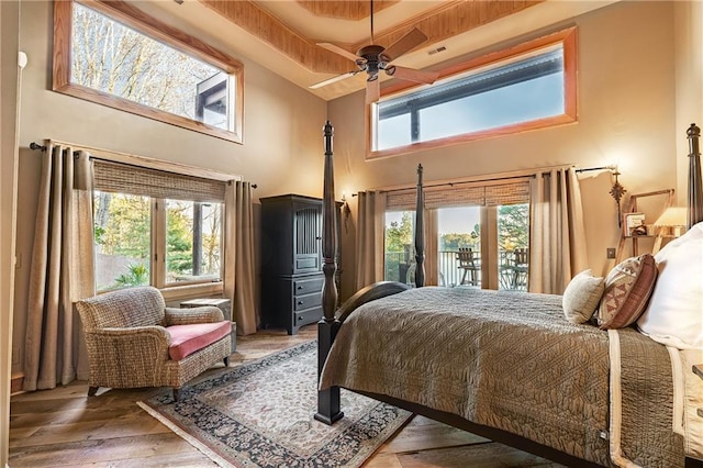 bedroom with multiple windows, light wood-type flooring, a high ceiling, and access to exterior