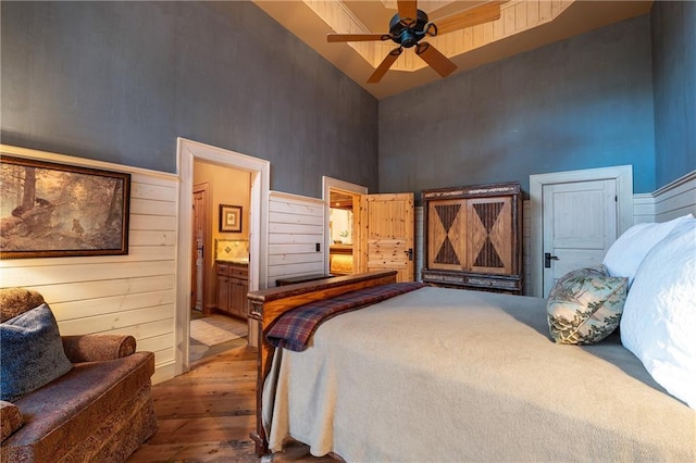 bedroom with wood walls, hardwood / wood-style floors, ensuite bath, a ceiling fan, and a high ceiling