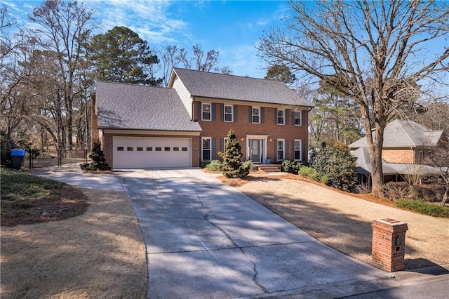 colonial home featuring a garage, brick siding, fence, driveway, and roof with shingles