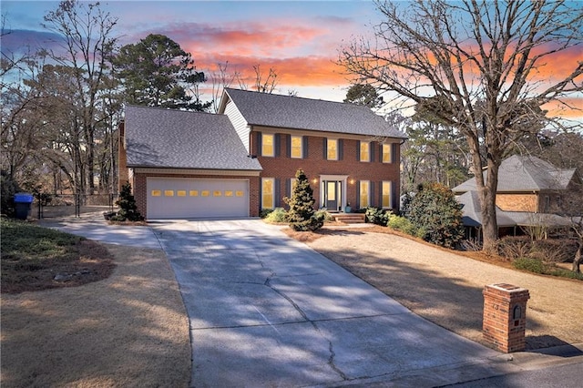 colonial-style house with a garage, concrete driveway, brick siding, and roof with shingles