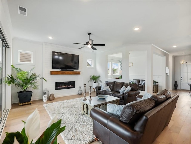 living room with ornamental molding, a fireplace, ceiling fan with notable chandelier, and light wood-type flooring