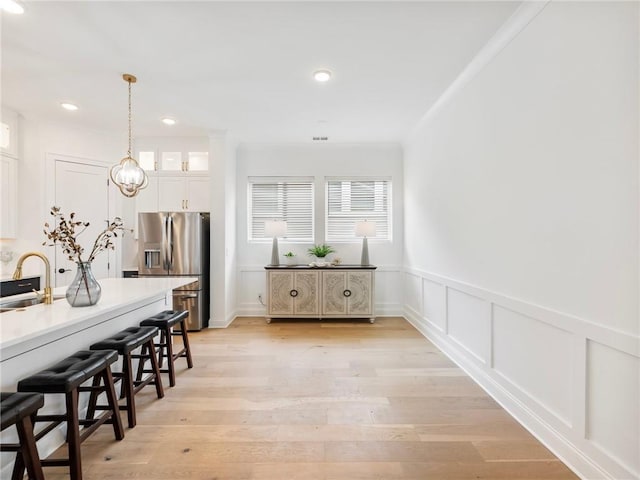 kitchen with pendant lighting, sink, a breakfast bar area, white cabinets, and stainless steel fridge with ice dispenser