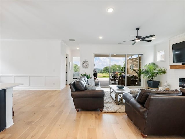 living room featuring crown molding, a large fireplace, ceiling fan, and light wood-type flooring