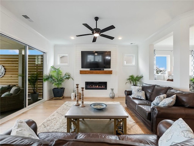 living room with ceiling fan, a large fireplace, and light hardwood / wood-style flooring