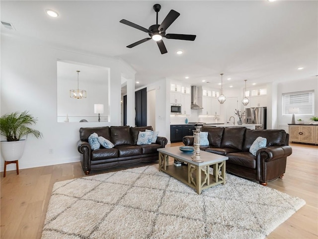 living room with sink, ceiling fan with notable chandelier, and light wood-type flooring