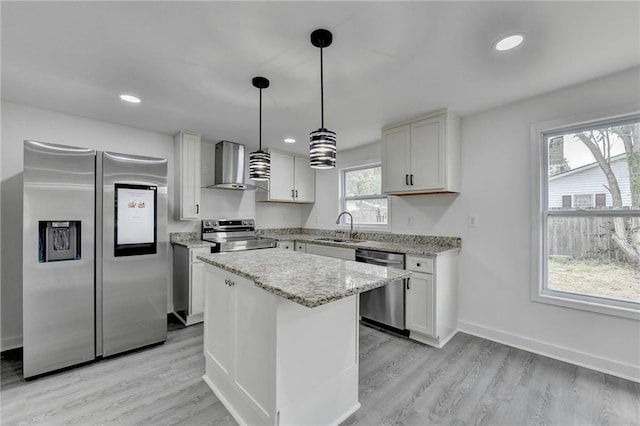 kitchen with a sink, a kitchen island, light stone countertops, appliances with stainless steel finishes, and wall chimney range hood