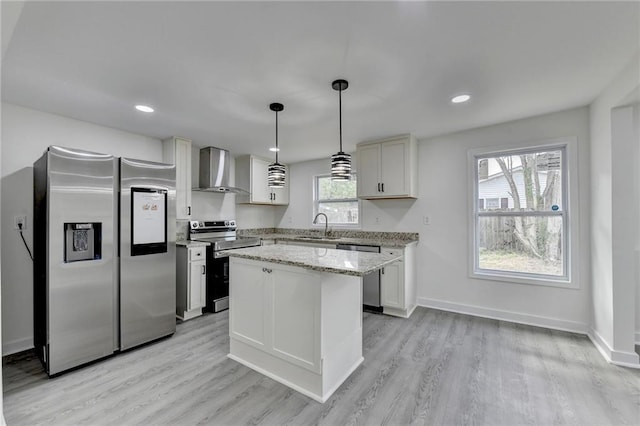 kitchen with stainless steel appliances, baseboards, a kitchen island, a sink, and wall chimney range hood