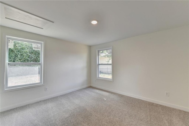 unfurnished room with baseboards, attic access, and light colored carpet